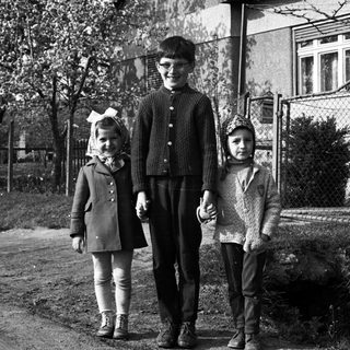Three children stand together outside a house in black and white.
