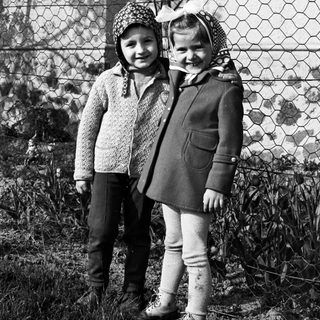 Two children stand outdoors near a fence in a black and white photo.
