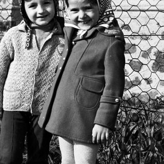 Two children stand outdoors near a fence in a black and white photo.