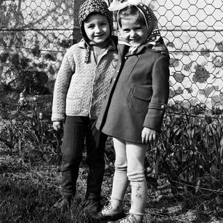 Two children stand outdoors near a fence in a black and white photo.