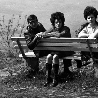 Black and white photo of people on a bench, hillside view.