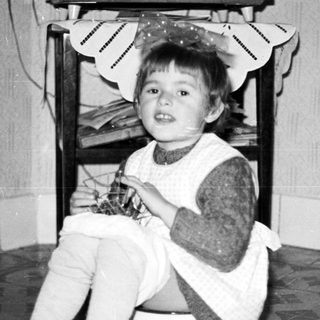 Black and white photo of a child seated near a chair.