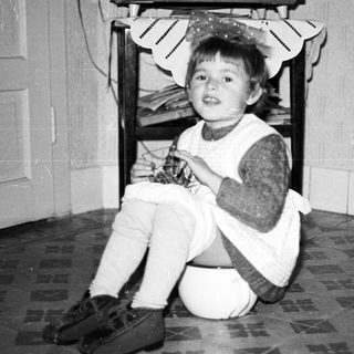 Black and white photo of a child seated near a chair.