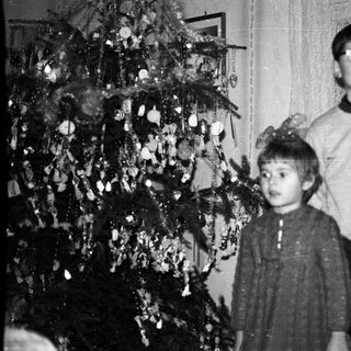 Two children stand near a decorated Christmas tree.