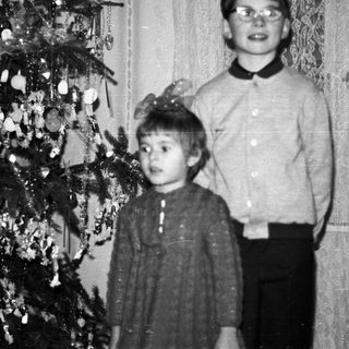Two children stand near a decorated Christmas tree.
