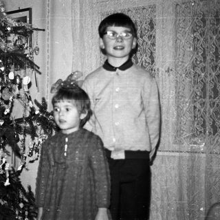Two children stand near a decorated Christmas tree.