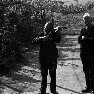 Two men, one playing violin, stand outdoors.