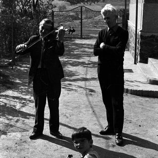 Musician plays violin while a boy watches, seated.