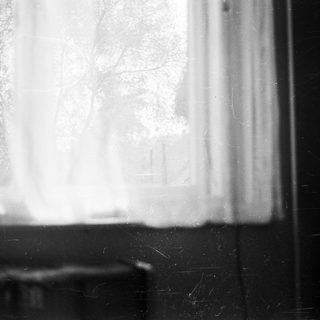 Dusty, dark room with a window and sheer curtain.