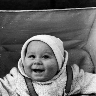 Baby in a vintage stroller, wearing a bonnet and overalls.