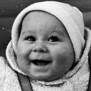 Baby in a vintage stroller, wearing a bonnet and overalls.