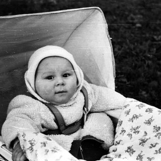 Baby in a vintage stroller, looking directly at the camera.