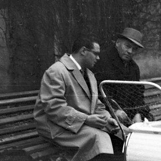 Man, baby in carriage, and another man in a park.