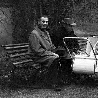 Man and child in stroller sit on park benches.