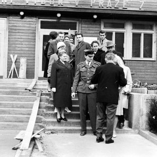 People exiting a building, guarded by a military officer.