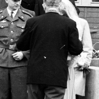 People exiting a building, guarded by a military officer.