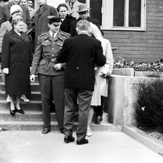 People exiting a building, guarded by a military officer.