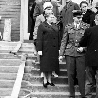 People exiting a building, guarded by a military officer.
