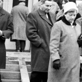 Group gathers outside a building, seemingly welcoming or escorting someone.
