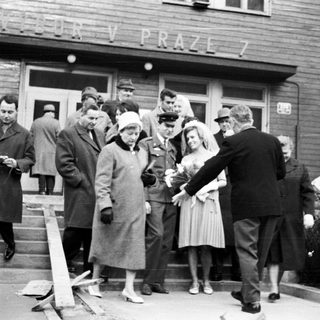Group gathers outside a building, seemingly welcoming or escorting someone.