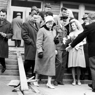 Group gathers outside a building, seemingly welcoming or escorting someone.
