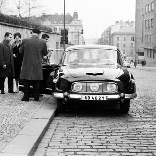 Group of people near a vintage car on a cobblestone street.