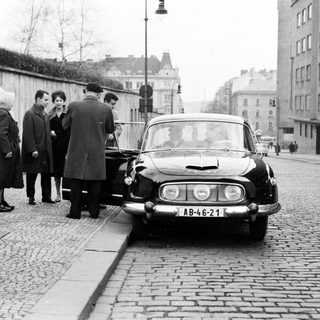 Group of people near a vintage car on a cobblestone street.