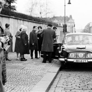 Group of people near a vintage car on a cobblestone street.