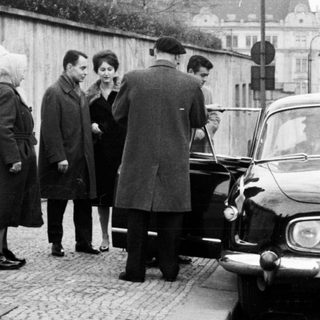 Group of people near a vintage car on a cobblestone street.