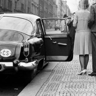 Military officer escorts women near a brick wall.