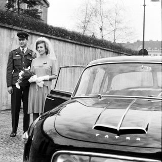 Military officer and bride stand near a vintage Tatra car.