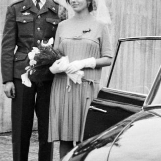 Military officer and bride stand near a vintage Tatra car.