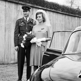 Military officer and bride stand near a vintage Tatra car.