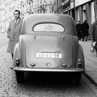Man stands next to a vintage car on a street.