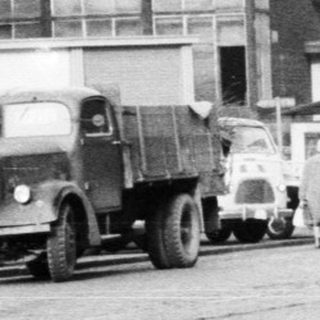 Man stands next to a vintage car on a street.