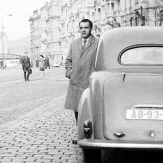 Man stands next to a vintage car on a street.