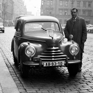 Man stands beside vintage car on a cobblestone street.