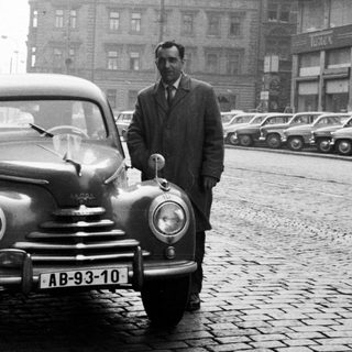 Man stands beside vintage car on a cobblestone street.