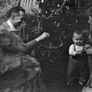 Family gathers near a Christmas tree, vintage photograph.