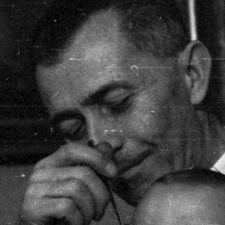 Man feeding a baby, with a woman seated nearby.
