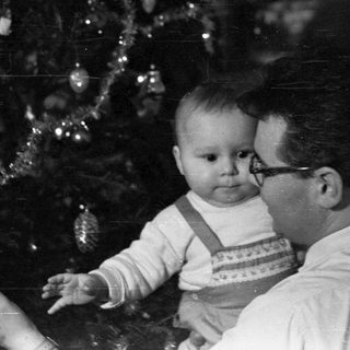 Man holds baby near a decorated Christmas tree.