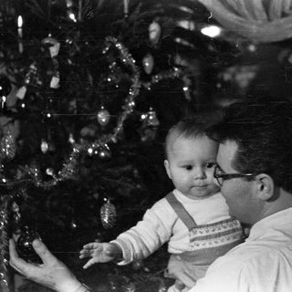 Man holds baby near a decorated Christmas tree.