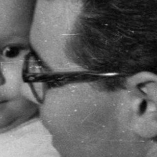 Man holds baby near a decorated Christmas tree.