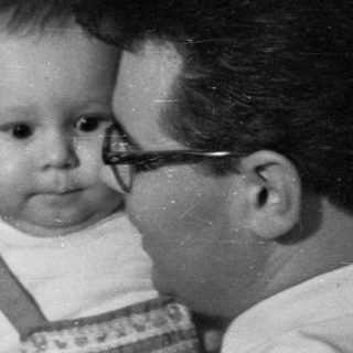 Man holds baby near a decorated Christmas tree.