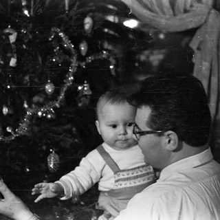 Man holds baby near a decorated Christmas tree.