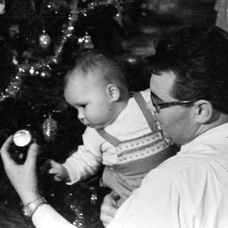 Baby being held near a decorated Christmas tree.
