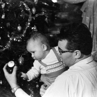 Baby being held near a decorated Christmas tree.