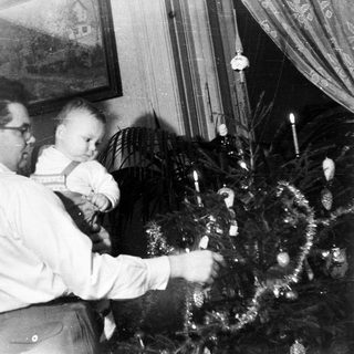 Man decorating a Christmas tree with a baby.