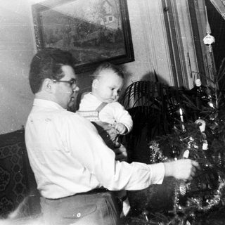 Man decorating a Christmas tree with a baby.