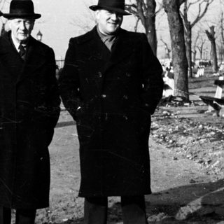 Two men in coats and hats stand outdoors.
